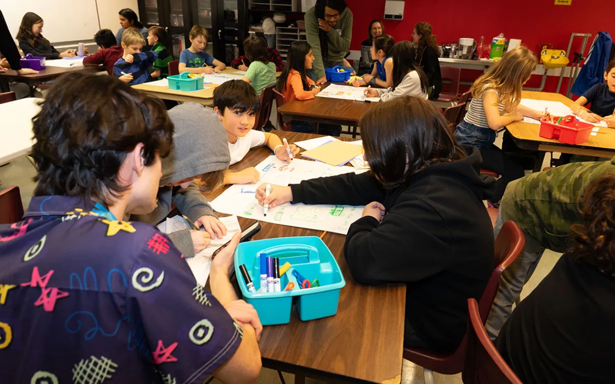 Students sit at tables in the Makerspace using markers to draw paper prototypes of games