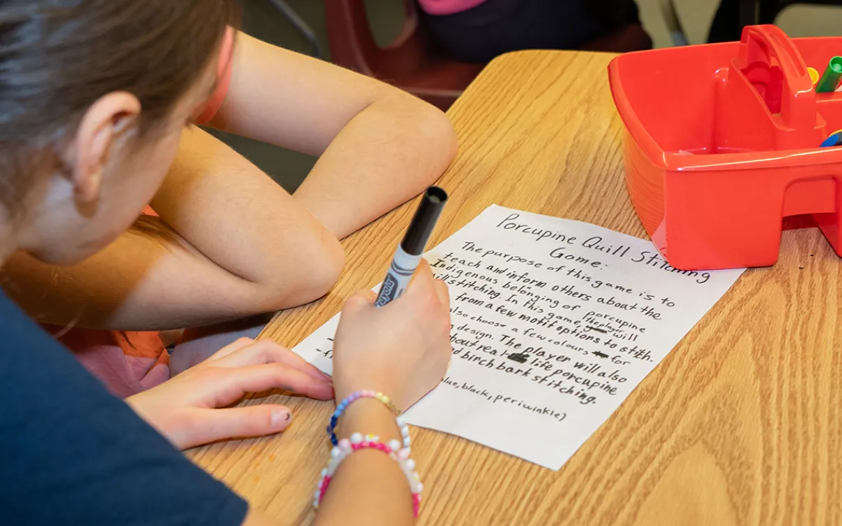 Students sitting at a table write a plan for a porcupine quill stitching game