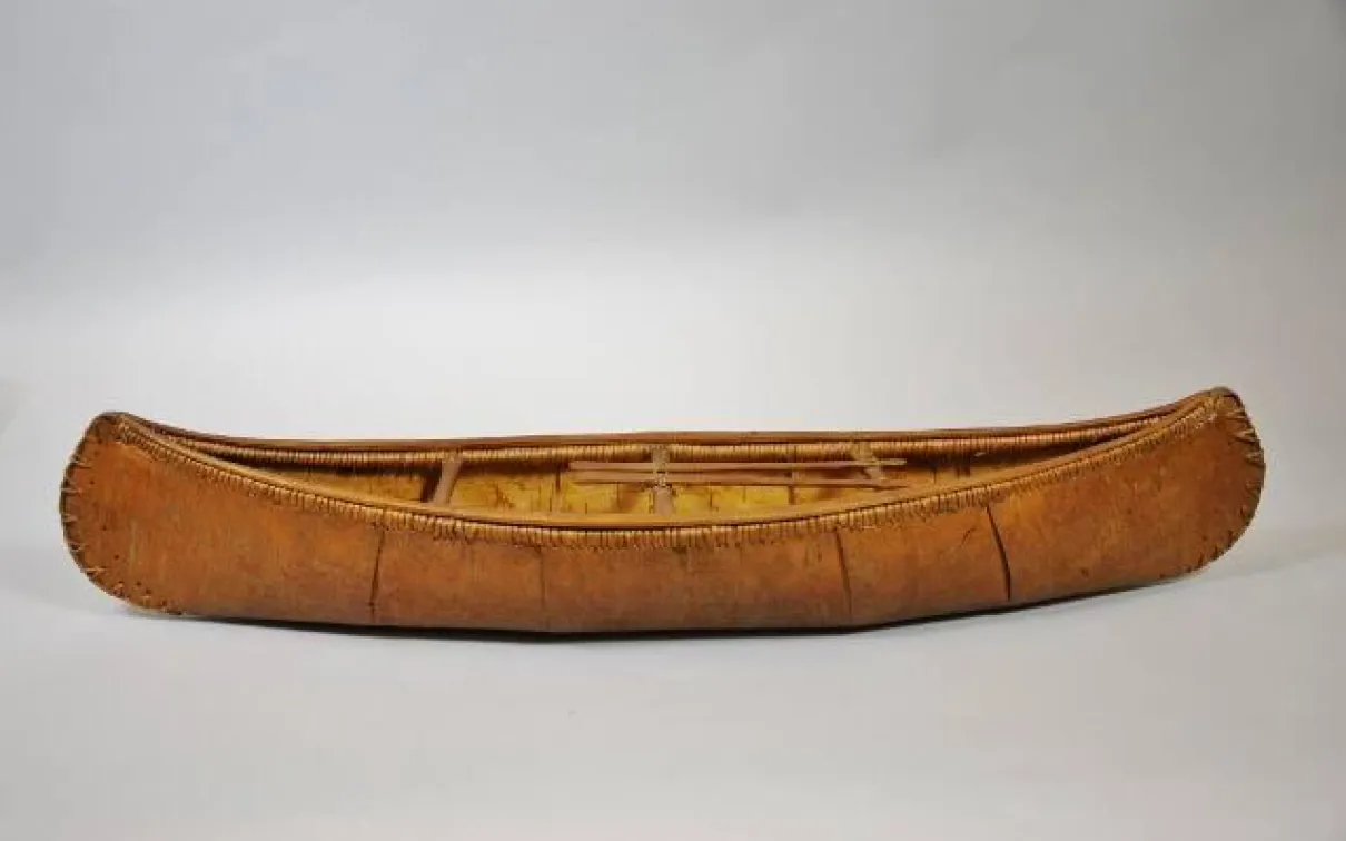A 68 cm model of a birch bark canoe, showing intricate and accurate details including spacers, paddles, and spruce root stitching the bark to the frame.