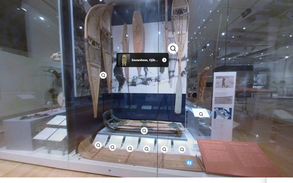 A case in a museum gallery filled with three pairs of snowshoes of differing sizes, two different styles of sled, and images of Indigenous peoples in snowy environments using what’s inside the case.