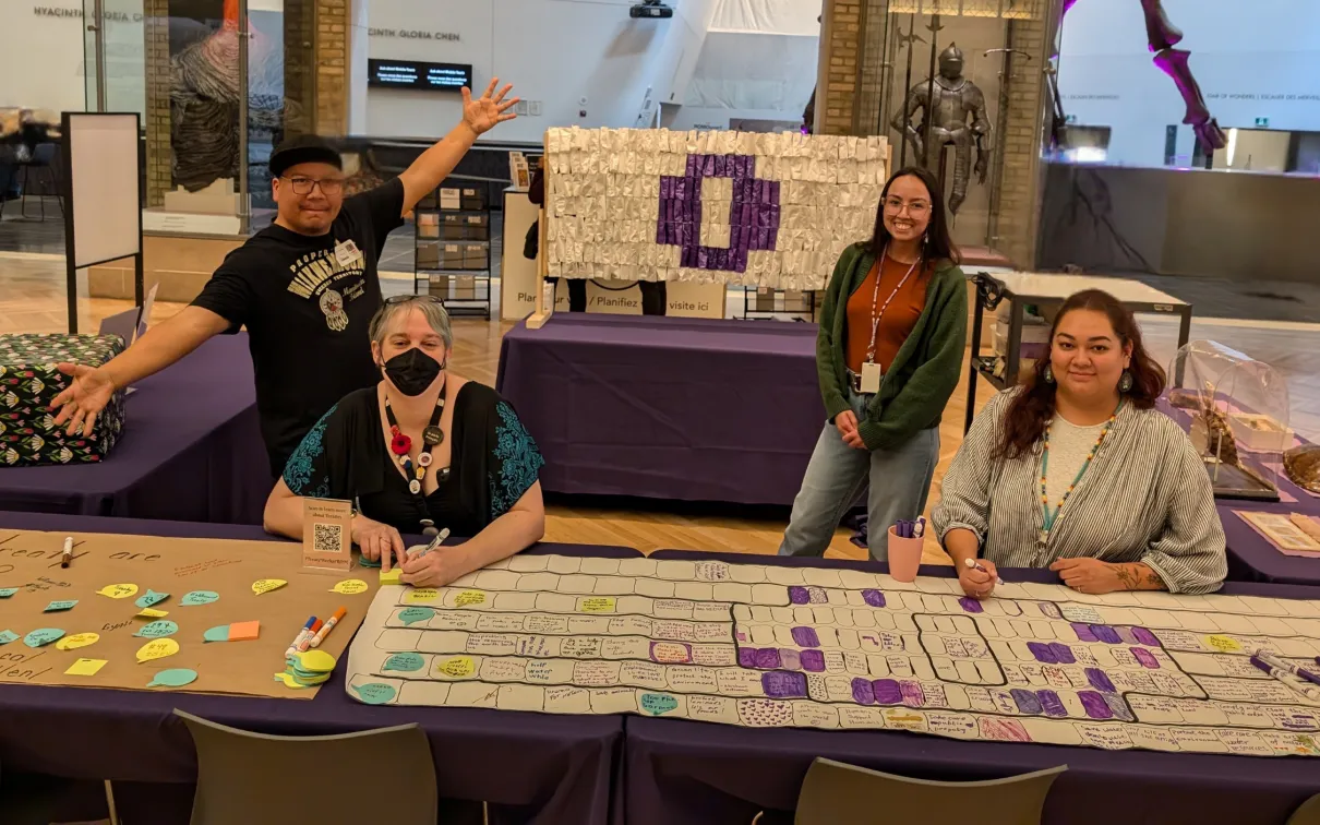Three indigenous staff members and one white staff member sit at a table full of activities smiling and gesturing around them.