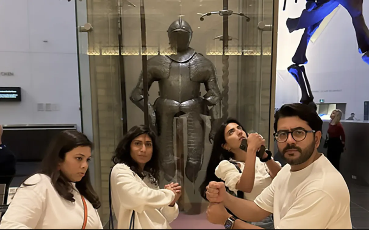 Four people posing in front of a knight's armor.