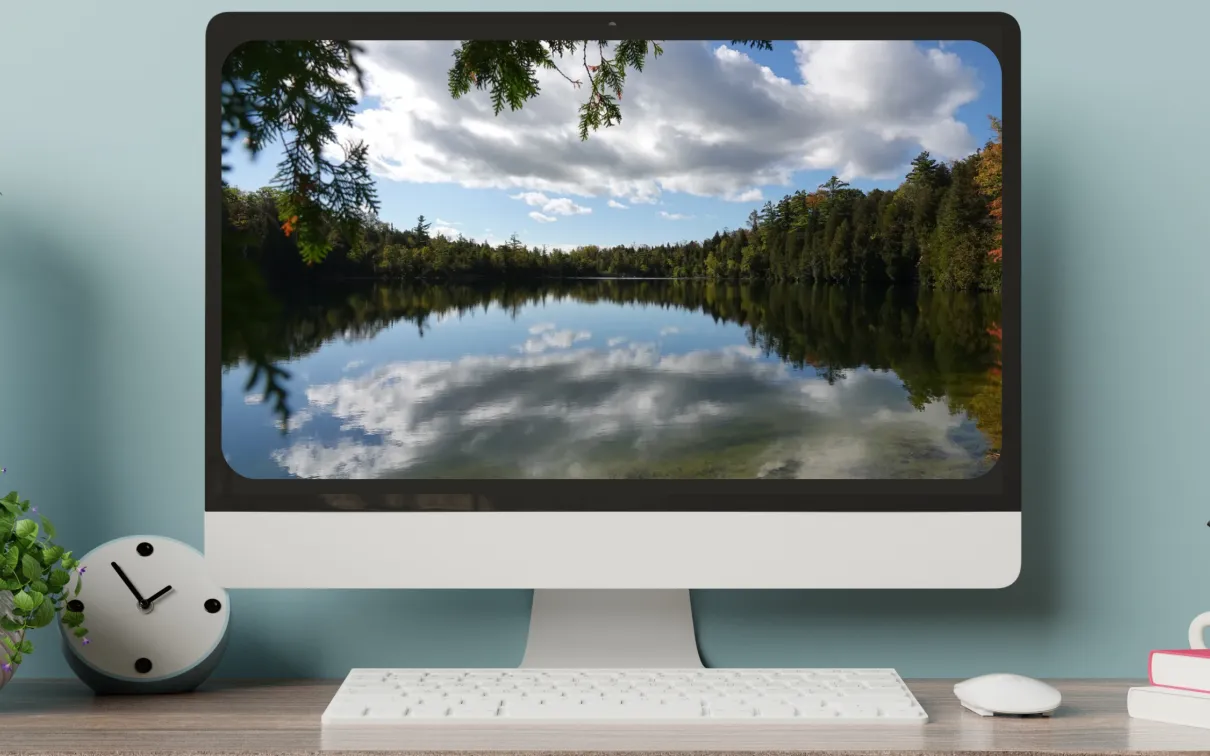 A computer screen on a desk displays an image of a glassy lake ringed by trees