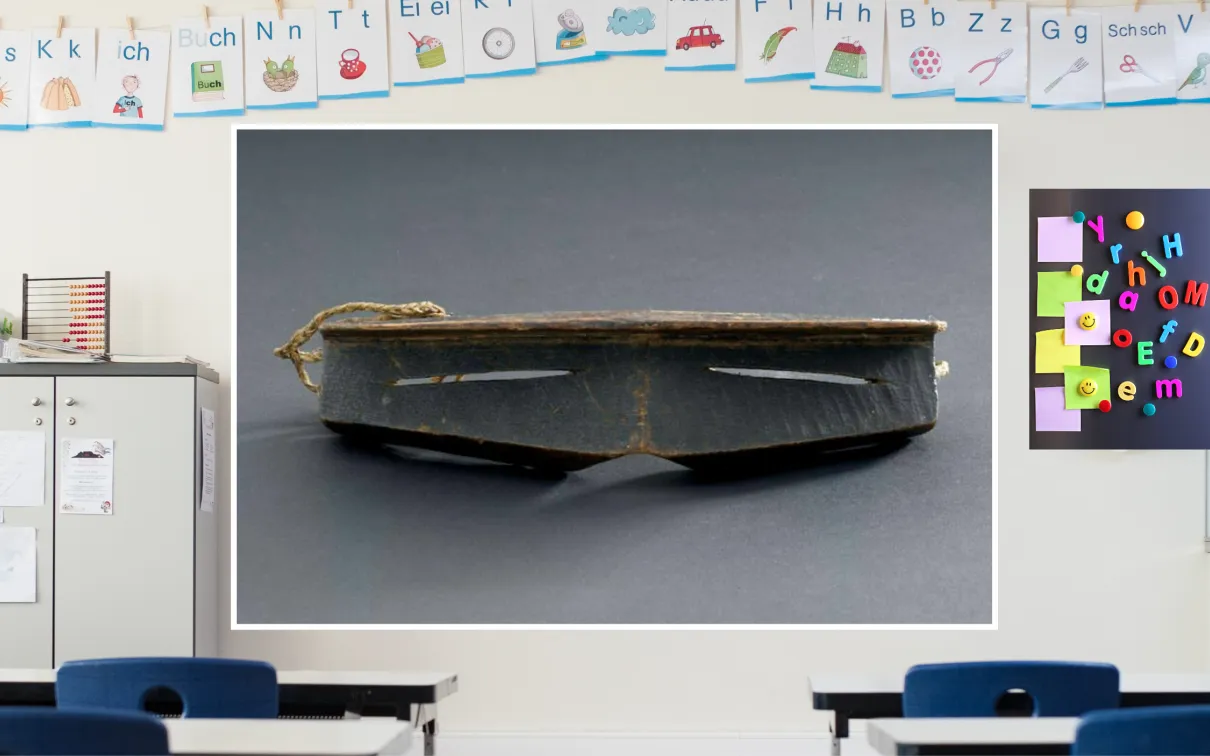 A colourful classroom with a display screen at the front. The screen shows iggaak (snow goggles) carved from wood with narrow horizontal slits for the eyes, and a string at the back.