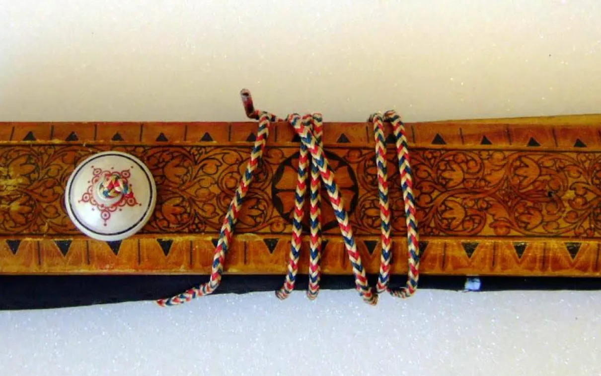 A decorative wooden case featuring circular and botanical designs. A white button on the top of the case secures a red, white ,nad blue cord wrapped around the case.
