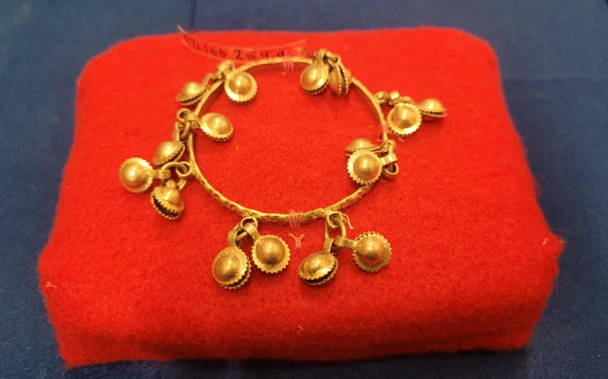 Round silver anklet for children. Thin silver central ring decorated with round silver charms suspended from central ring in eight groups of two. Produces jingling sound when handled or worn.