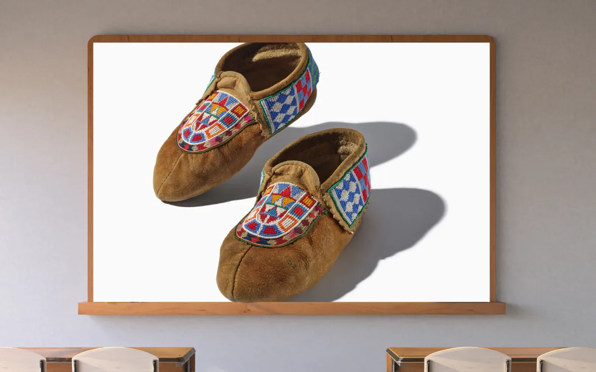 A screen in a classroom displays a pair of hide moccasins with colorful beading.