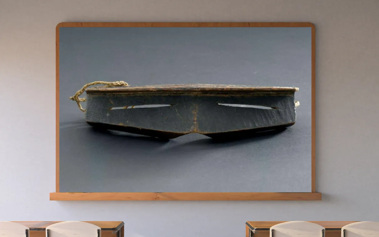 A classroom with a display screen at the front. The screen shows iggaak (snow goggles) carved from wood with narrow horizontal slits for the eyes, and a string at the back.