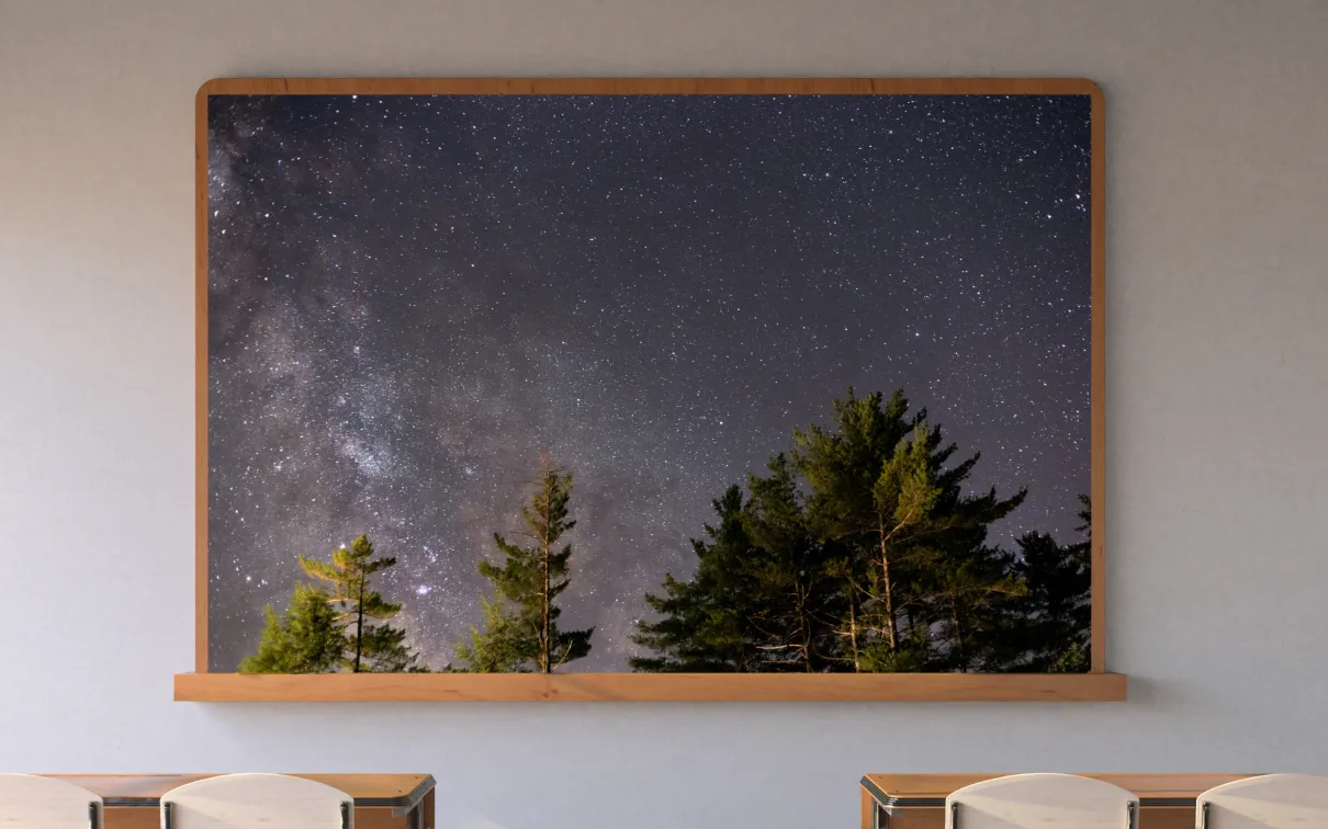 A screen in a classroom displays an image of the starry night sky framed by trees.