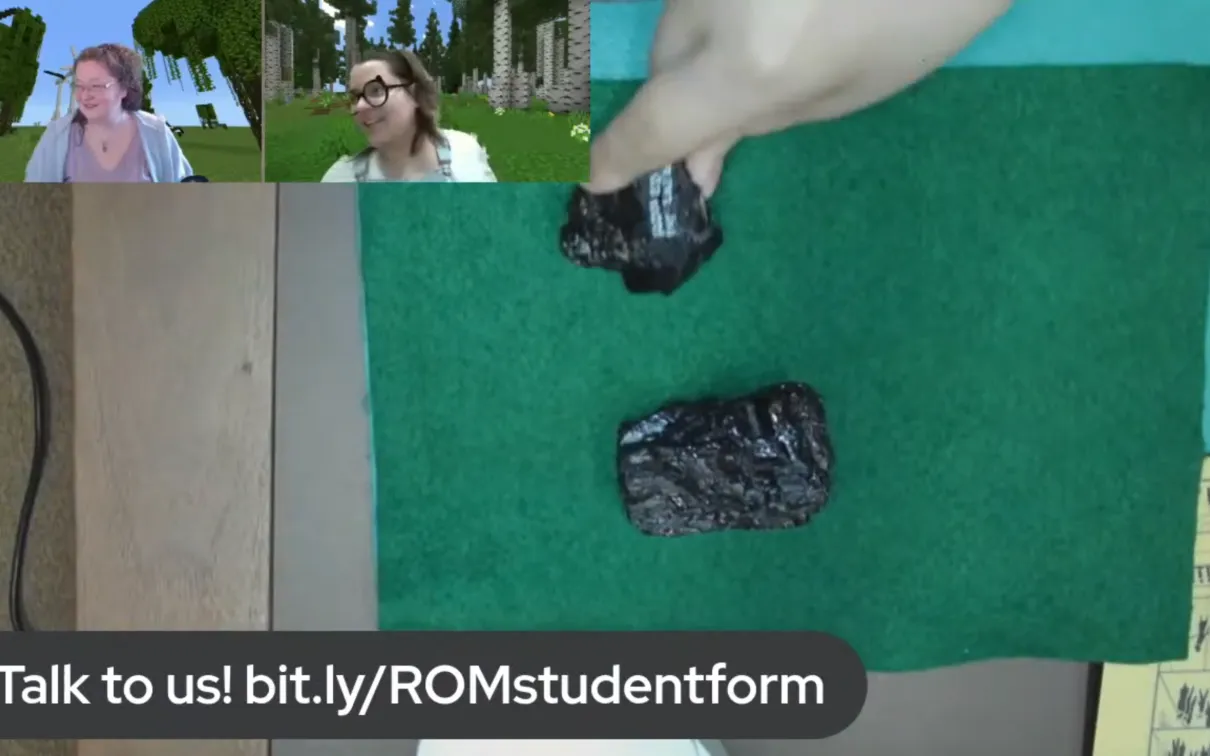 A desktop view of two pieces of coal on green felt. Two facecams of smiling women are in the top right of the image.
