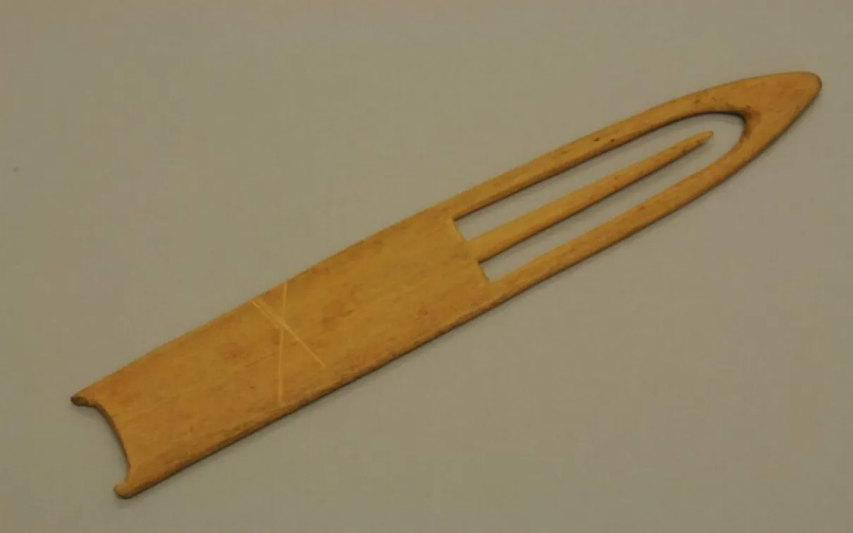 A carved piece of wood with a pointed tip and a pointed needle within a cutout space at the tip.