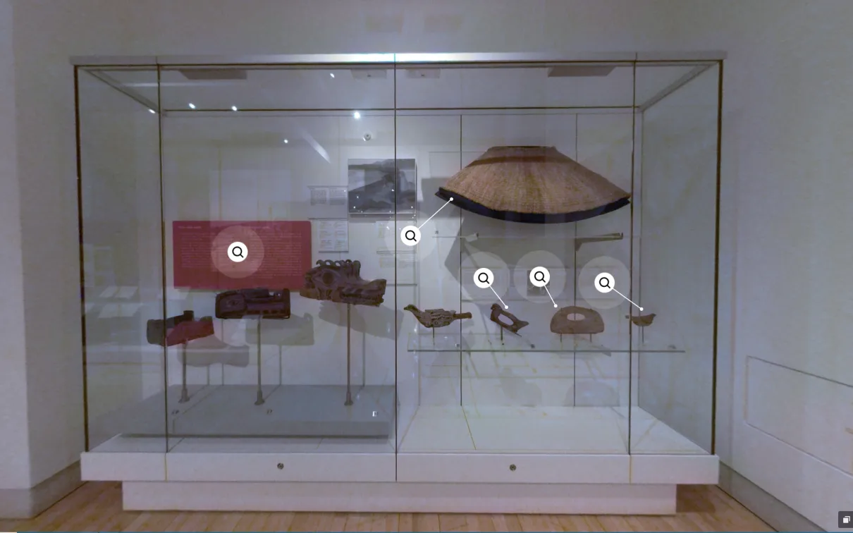 A case in a museum displaying many belongings made from cedar, including a cape, masks, and several tools.