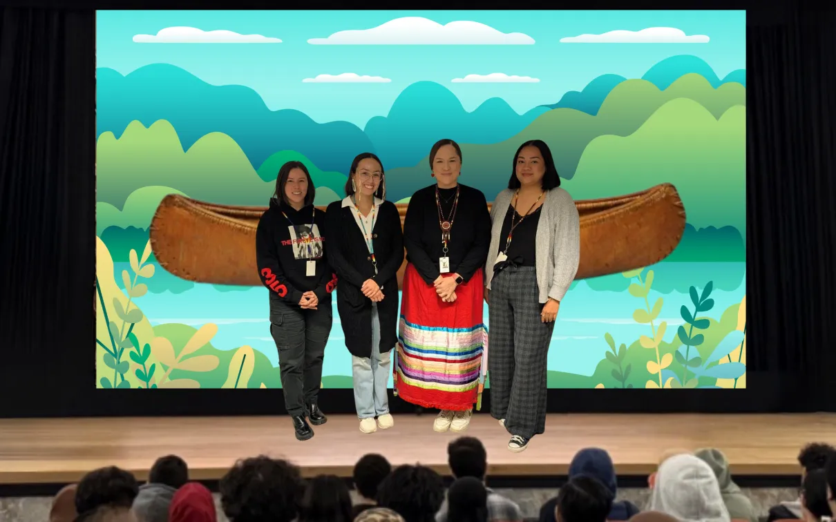 Four Indigenous women stand on a stage. The screen behind them displays an image of a canoe on an illustrated river.