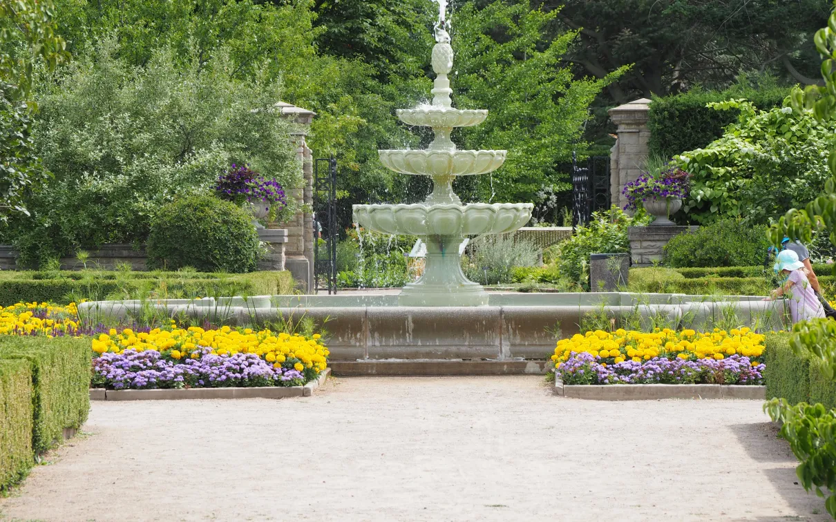 Fountain in background with flowers and walking path in foreground.