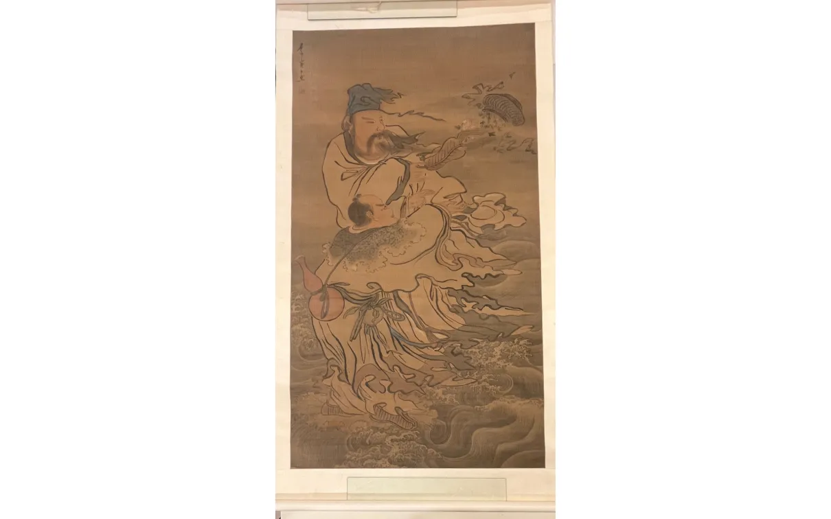 Vertical hanging scroll painting depicting two robed figures amid swirling water and wind. A taller figure stands above, wearing layered robes and a head covering, with long ribbons and sleeves flowing outward. Below, a smaller figure is carried or supported, partially wrapped in the taller figure’s garments. Waves and curving lines fill the lower half of the composition, suggesting movement through water, while fish-like forms and drifting elements appear near the upper right. The artwork is rendered in mu