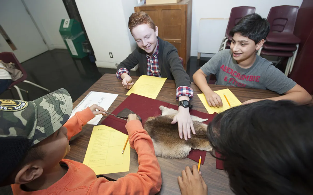 A smiling student touches muskrat fur while his classmates look on.