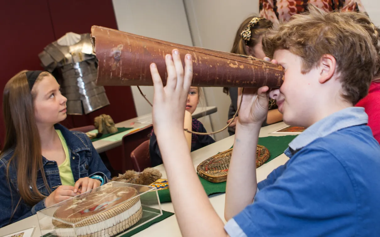 A student holds a birch bark moose call up to his eye while attempting to discern what it is.