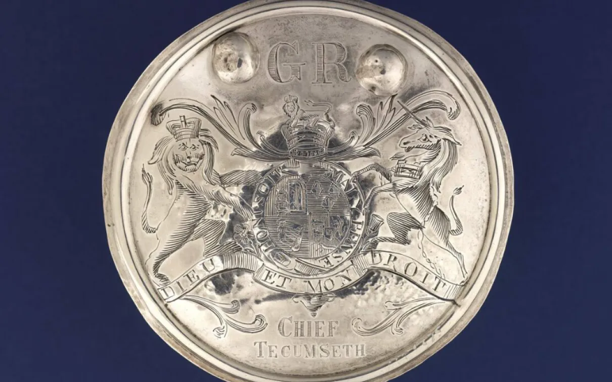 Round silver belt buckle with a coat of arms engraved in the centre, the letters G R at the top, and Chief Tecumseth at the bottom.