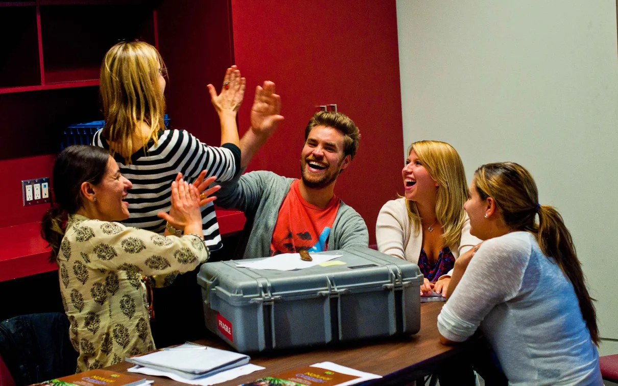 Teachers laugh and give each other high-fives around a table
