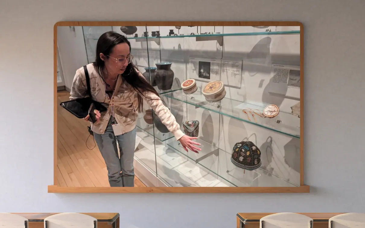 A screen on a classroom wall shows an Indigenous Museum Educator in the First Peoples Gallery at ROM