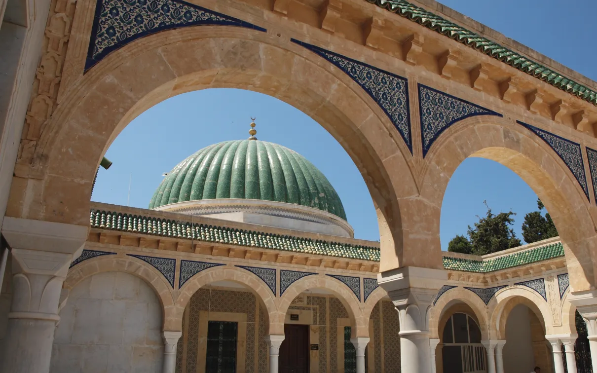 A beautiful, ornately decorated Islamic building with a domed roof and a blue tiled interior, under a clear blue sky.