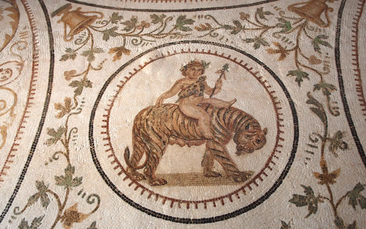 A mosaic featuring a central figure of a young boy riding a tiger, surrounded by intricate floral and geometric patterns