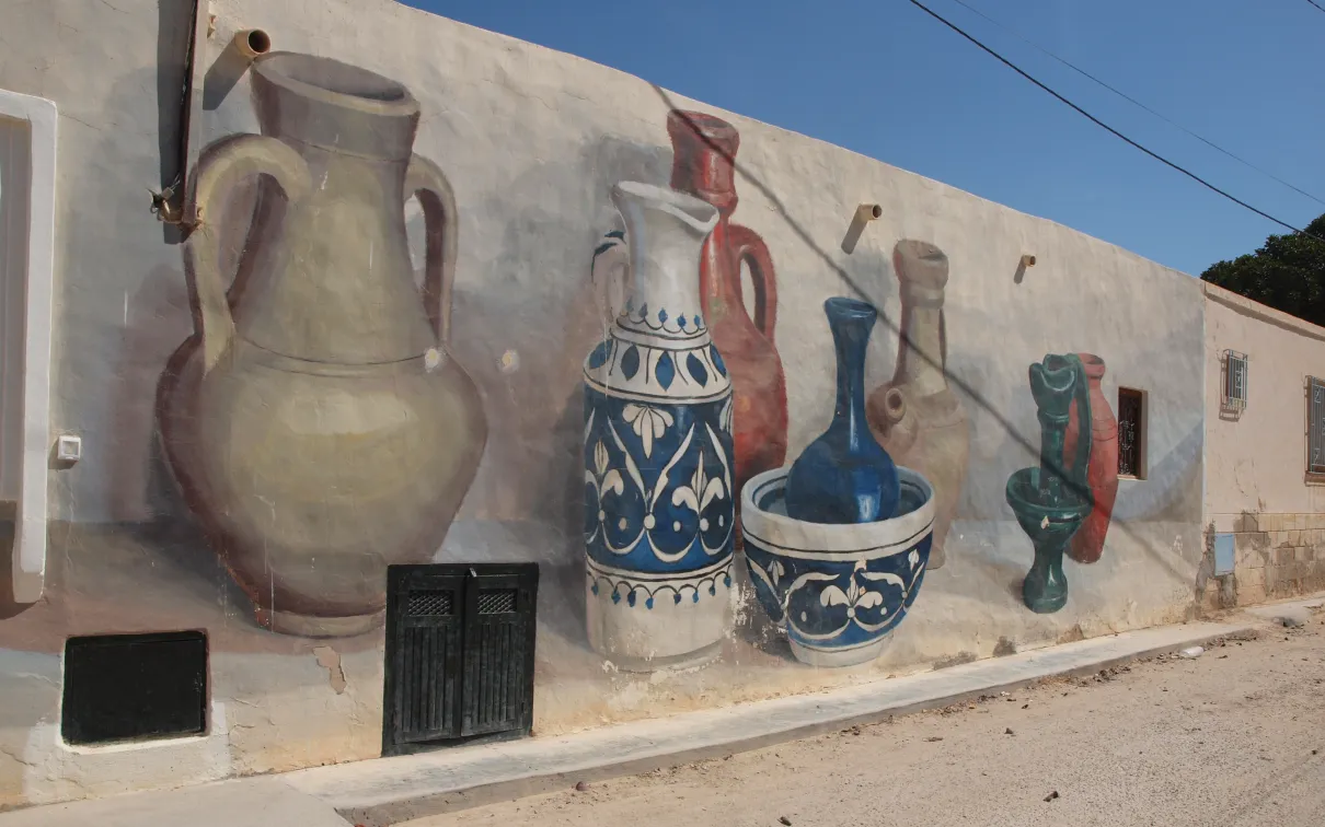A wall mural featuring colourful, hand-painted ceramic jugs arranged in a symmetrical, abstract pattern against a clear blue sky.