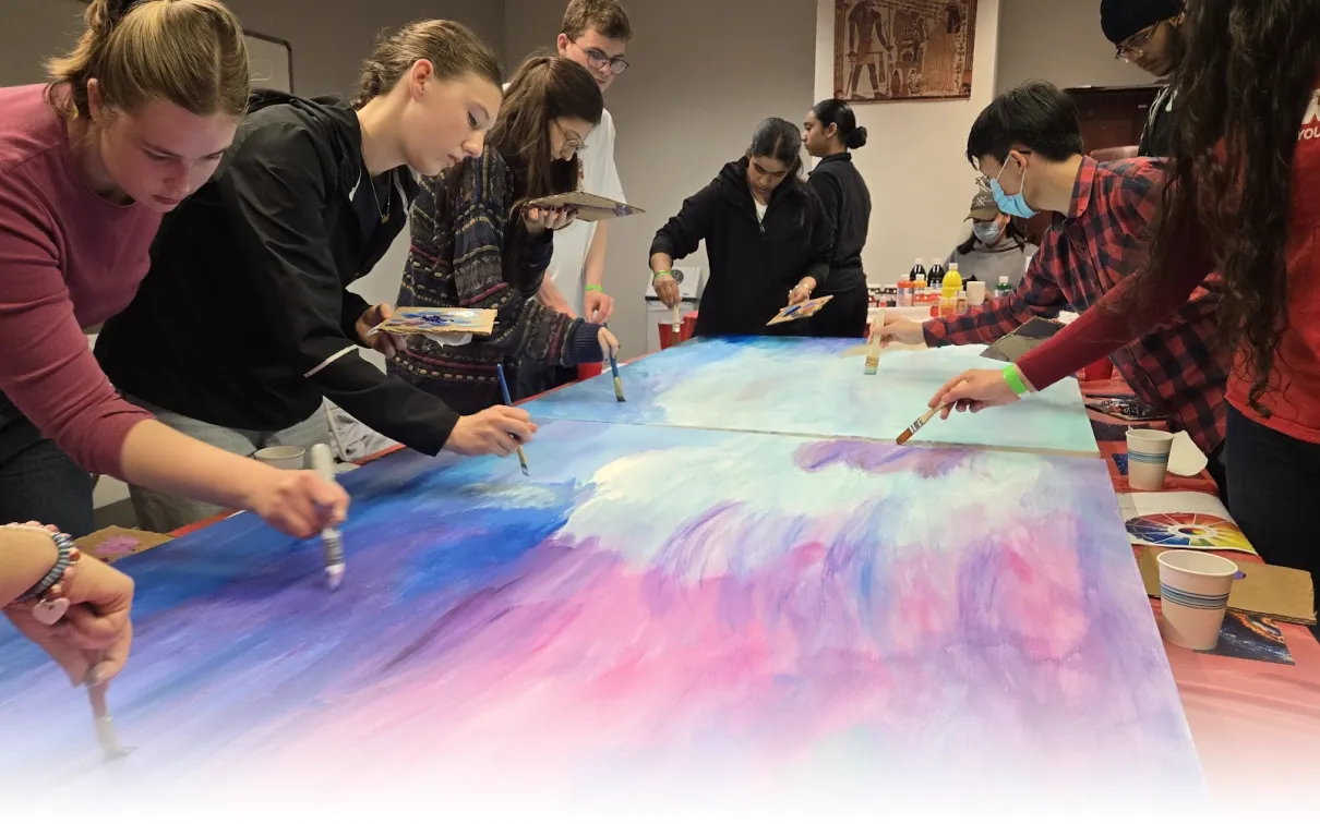 A group of Youth Cabinet members work together to paint a canvas with shades of blue, purple and pink.