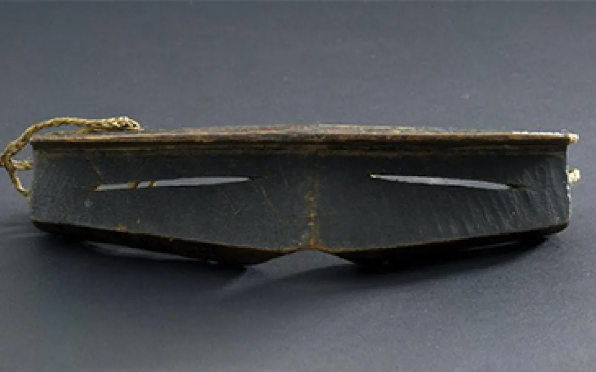 Iggaak (snow goggles) carved from wood with narrow horizontal slits for the eyes, and a string at the back.