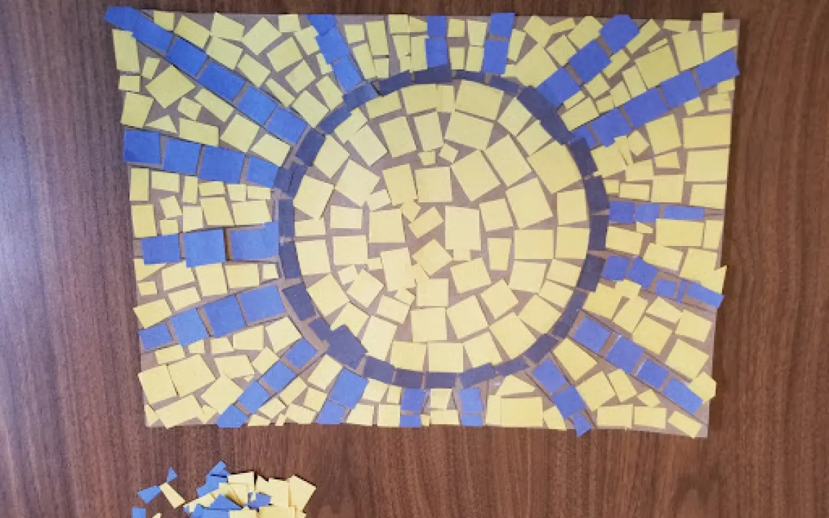 Mosaic of a sun made from yellow, blue, and black squares.
