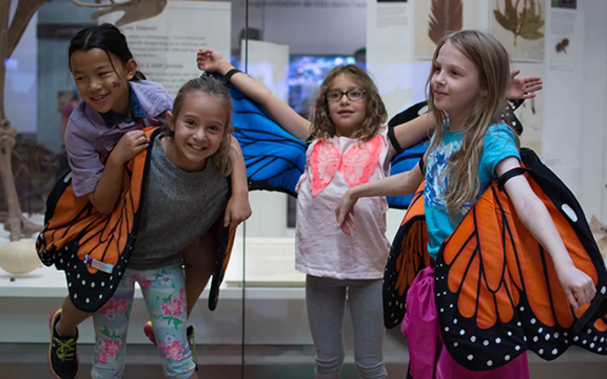 Four children stand with monarch wing costumes in front of an exhibit in the Schad Gallery at the ROM. Photo by Fatima Ali
