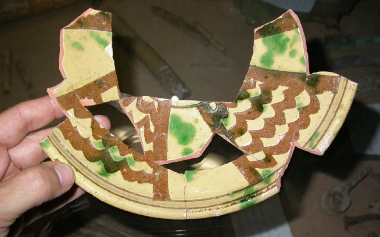 Pottery with an earthenware fired-clay body, overall white slip, incision through the slip with a broad tool, overall lead glaze, splashed with copper-green, probably mid-14th century.
