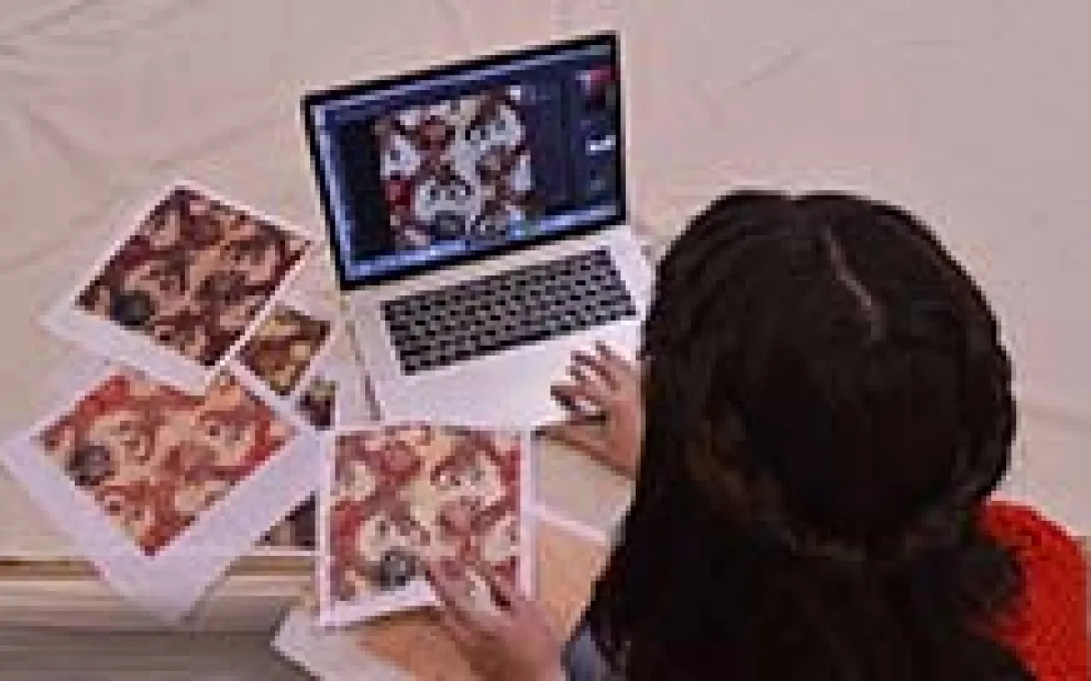A young woman sits in front of a laptop computer surrounded by squares of patterned fabric.
