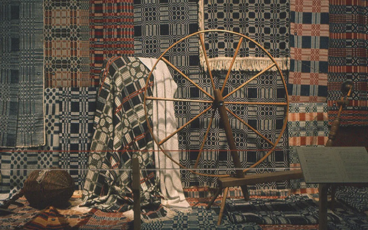 Photograph of textiles behind a spinning wheel

