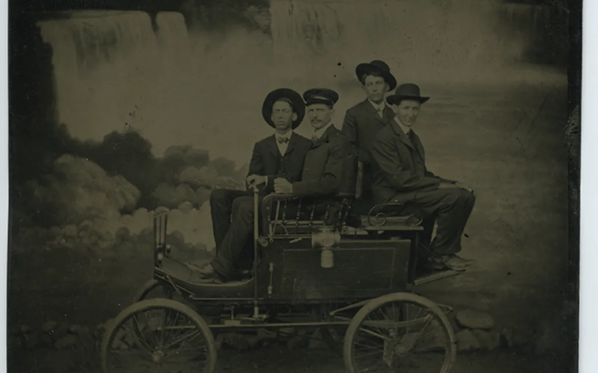 Photo de ferrotype noir et blanc de quatre hommes assis sur un chariot devant les chutes du Niagara

