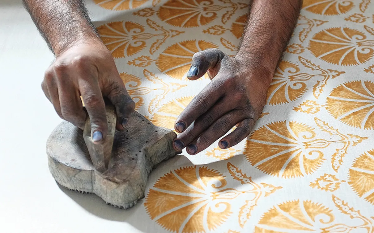 Hands pressing a stamp with yellow paint onto white fabric.