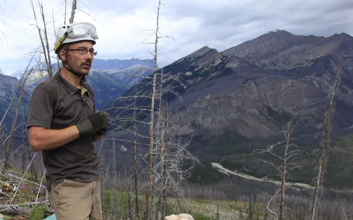 Jean-Bernard Caron standing on a hill with mountains in the background