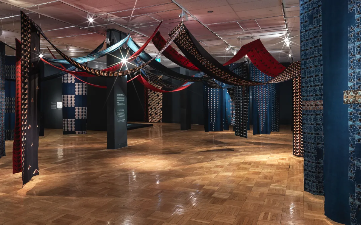 Vue panoramique d'une installation de sculpture souple composée de longueurs de tissu de coton imprimé suspendues en hauteur.