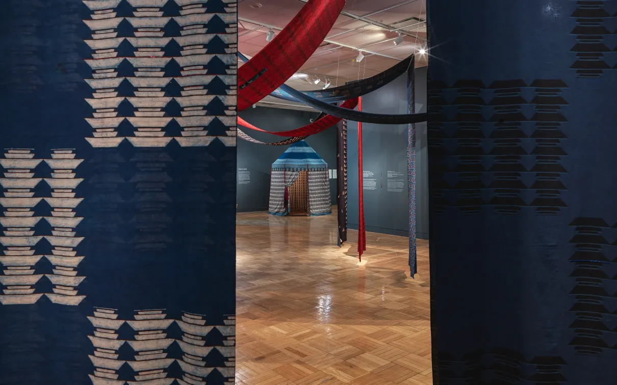 Vue d'une structure de tente en coton à travers une ouverture dans deux panneaux de coton imprimés et suspendus, dans l'exposition Swapnaa Tamhane : Mobile Palace, au ROM.