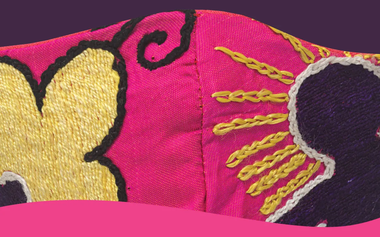 Detail of pink cloth mask with embroidered figures in black and yellow.