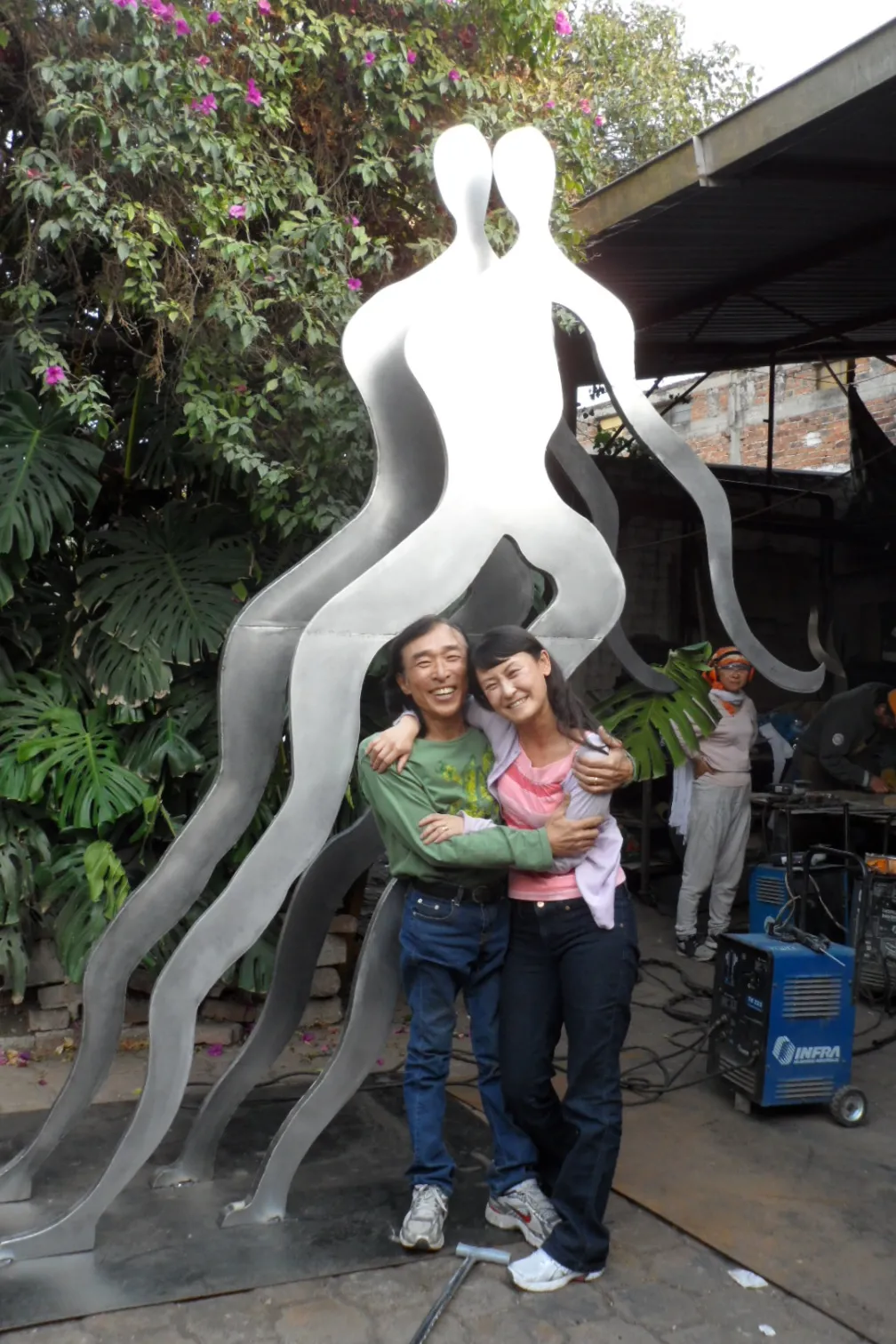 A photo of Won Lee and his wife, Hyon Chu Lee, standing in front of a large-scale artwork titled "Meditators." The piece, which is 80 inches tall, is on permanent display at Vermont State University.