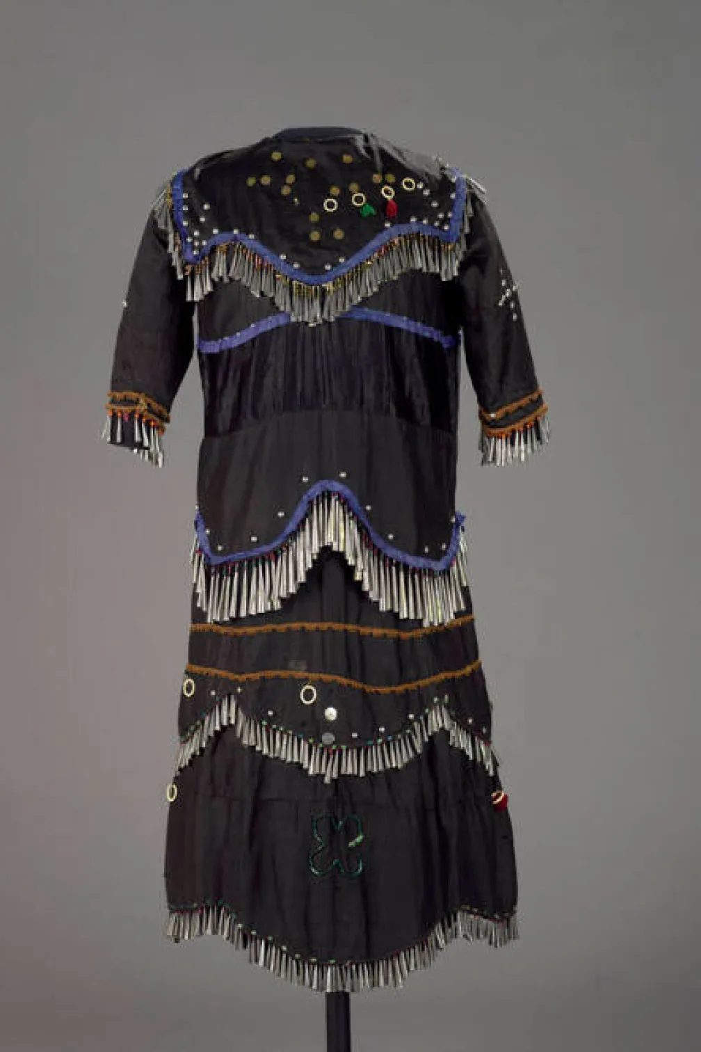 A dress made of dark fabric decorated with many fringes of metal cones.