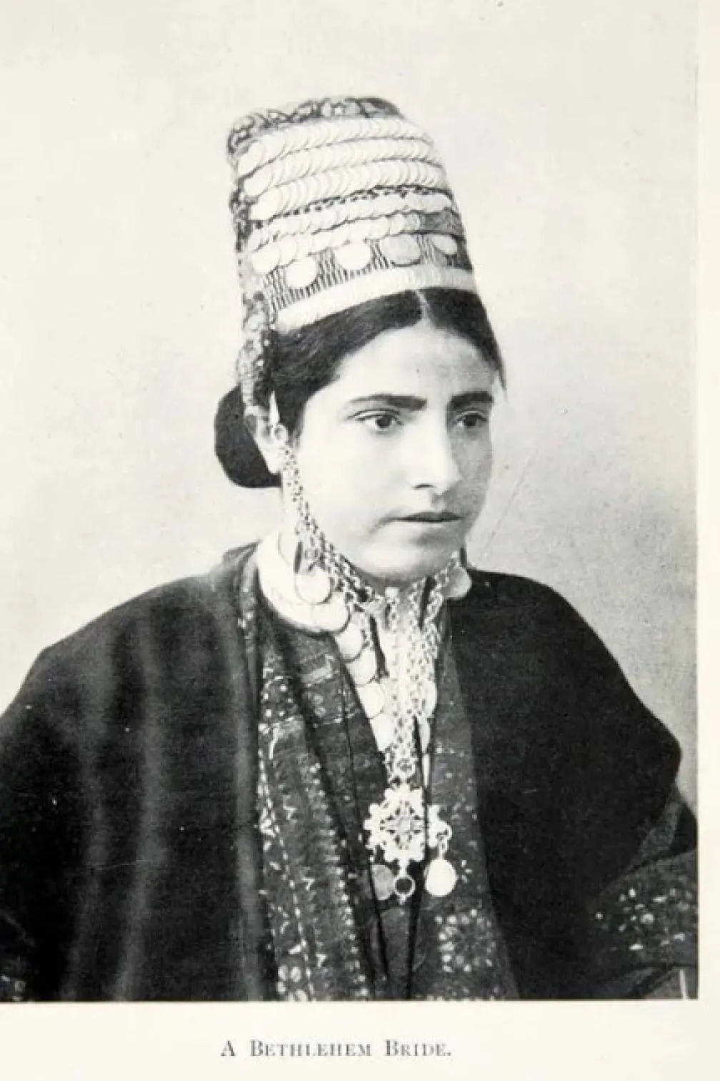 A bride from Bethlehem wears a coin headdress (shatweh) atop her head, held in place   with an elaborate chin-chain (iznaq). Photograph (reproduction), 1904. Photo © ROM