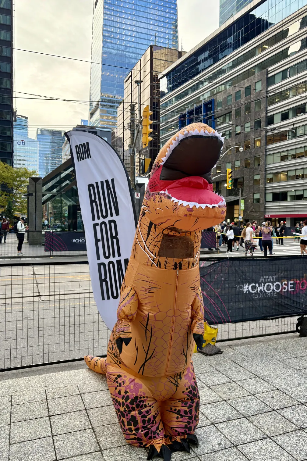 Introduce an inflatable dinosaur mascot as the official Run for ROM mascot, greeting participants at the 5K start line and cheering them on throughout the event. 