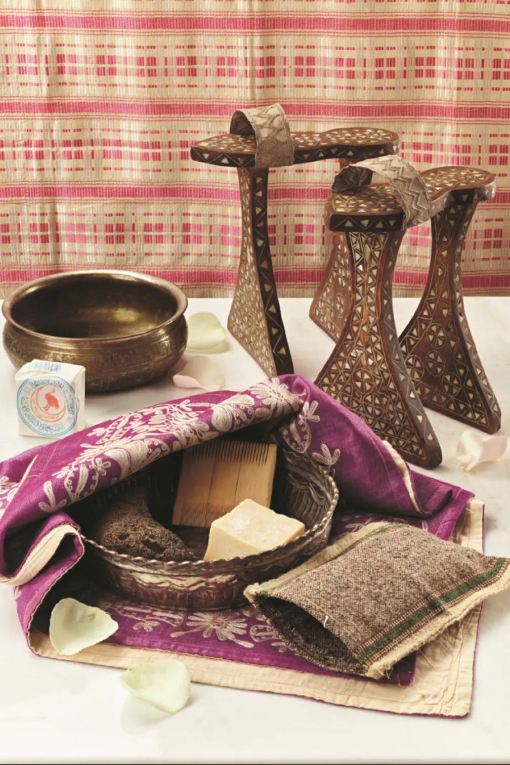 Traditional grooming items arranged on embroidered fabric, including carved wooden platform sandals, a metal basin, soap, a comb, and woven textiles.