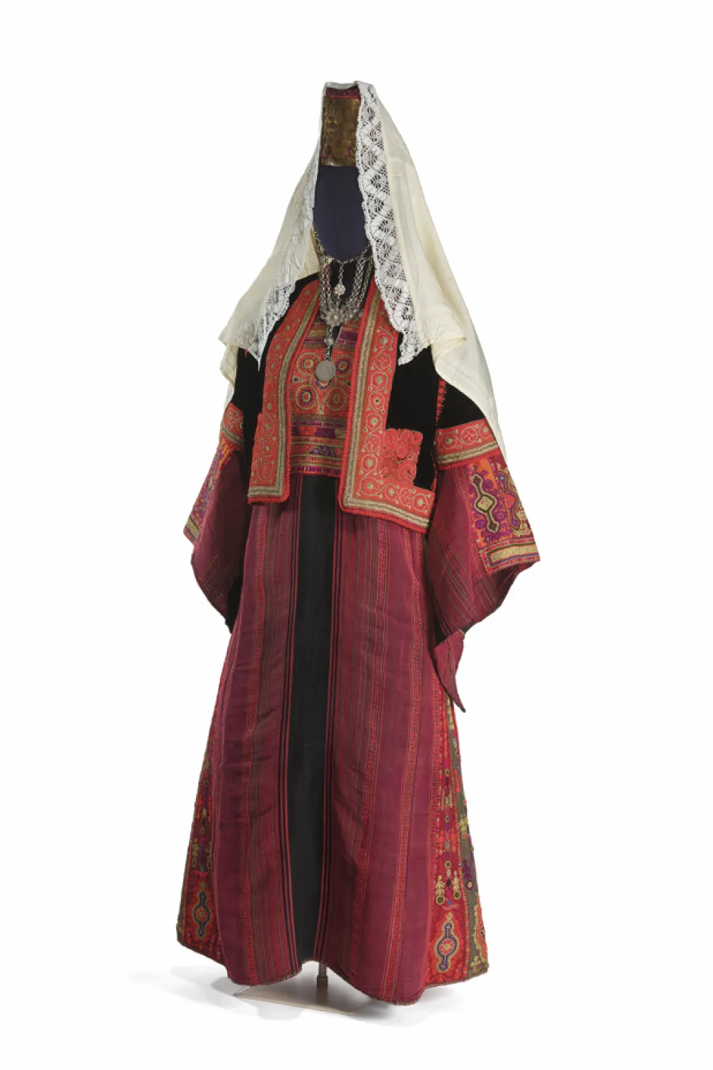 Traditional embroidered red robe with ornate detailing, layered silver jewelry, and a white lace-trimmed head covering displayed on a mannequin.