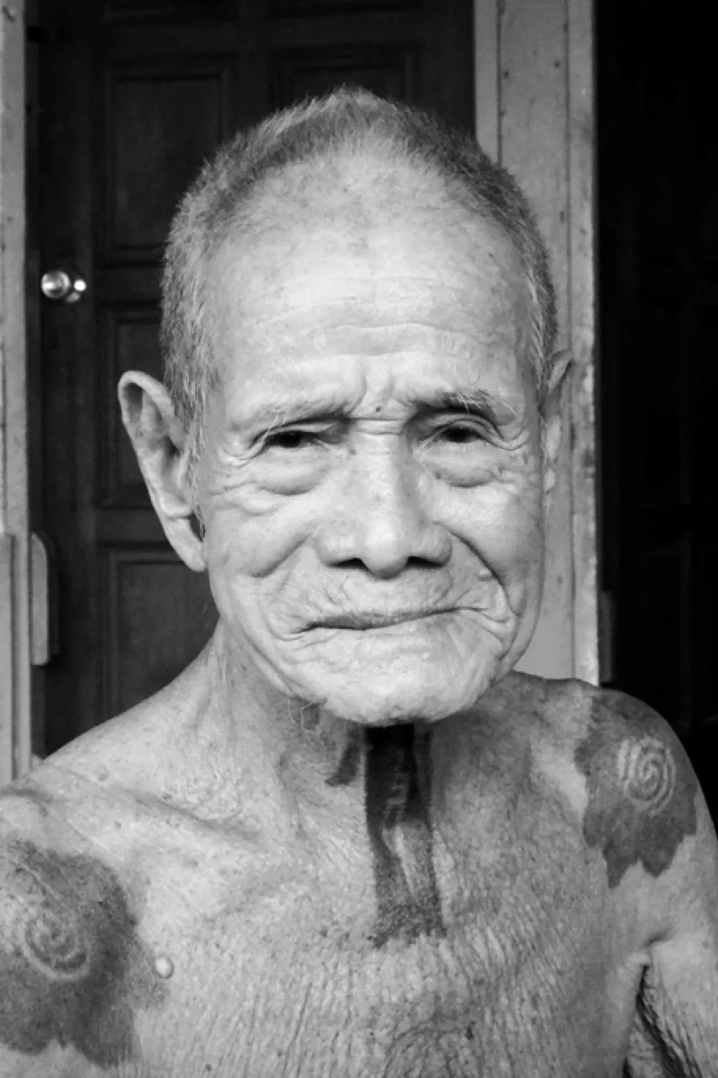 Black and white photograph of an older man with tattoos on his neck and shoulders
