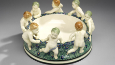 A colourful earthenware bowl with figures of putti dancing around outter rim.