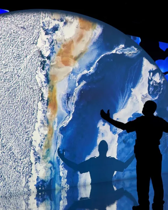 Projection d'une planète avec la silhouette d'un homme les mains en l'air regardant une grande projection d'une planète