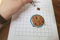 Chocolate chip cookie on grid paper, toothpick on paper. Paperclip in hand, moving chocolate chips into a separate pile.